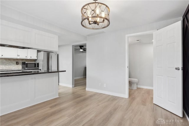 kitchen with stainless steel appliances, white cabinetry, light wood finished floors, dark countertops, and tasteful backsplash