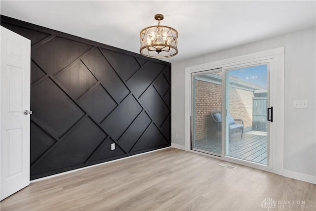 spare room featuring baseboards, light wood-style floors, visible vents, and a notable chandelier