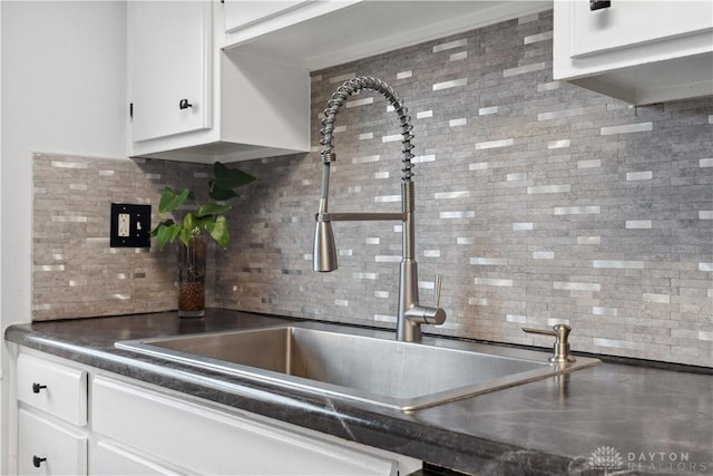 kitchen with dark countertops, white cabinetry, decorative backsplash, and a sink