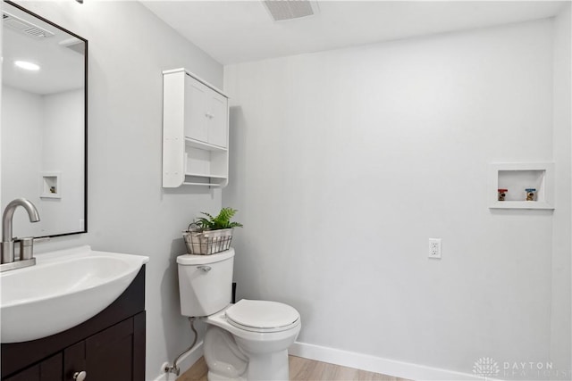 bathroom with baseboards, visible vents, toilet, wood finished floors, and vanity