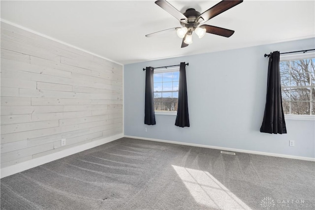 empty room with wood walls, a ceiling fan, visible vents, baseboards, and carpet