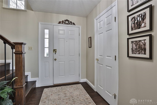 entrance foyer with a textured ceiling, dark wood-type flooring, stairway, and baseboards