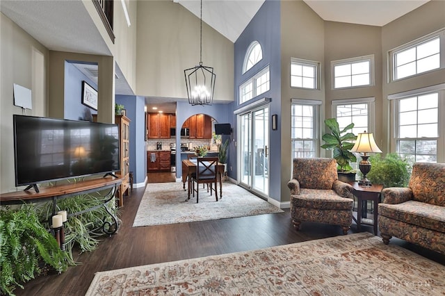 living area featuring a chandelier, dark wood-style flooring, a towering ceiling, and baseboards