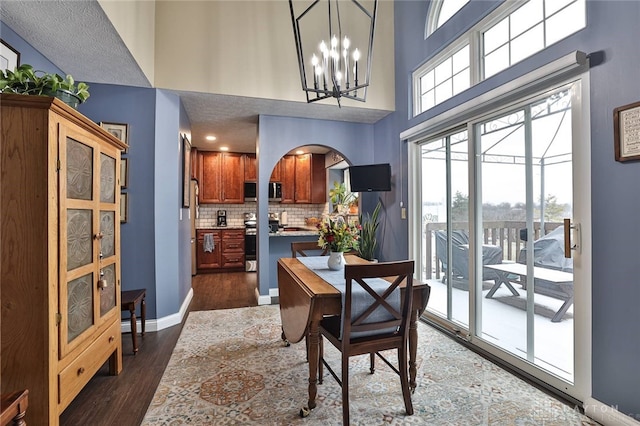 dining space with arched walkways, dark wood-style flooring, a notable chandelier, a high ceiling, and baseboards