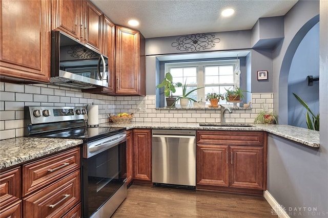 kitchen with light stone counters, dark wood-style flooring, backsplash, appliances with stainless steel finishes, and a sink