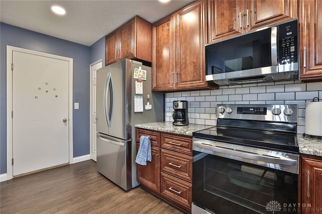 kitchen with baseboards, dark wood finished floors, light stone counters, appliances with stainless steel finishes, and backsplash