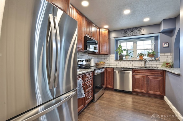 kitchen featuring tasteful backsplash, appliances with stainless steel finishes, dark wood-type flooring, a sink, and light stone countertops