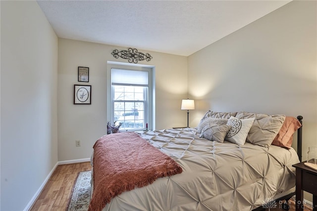 bedroom featuring light wood-style flooring, baseboards, and a textured ceiling