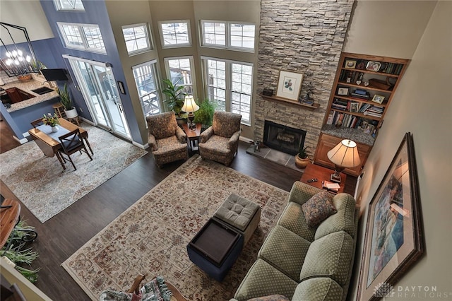 living area featuring a towering ceiling, baseboards, wood finished floors, and a stone fireplace