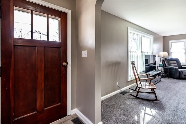 carpeted entryway featuring arched walkways, visible vents, and baseboards