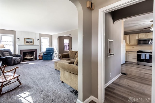 living room featuring visible vents, baseboards, arched walkways, wood finished floors, and a brick fireplace