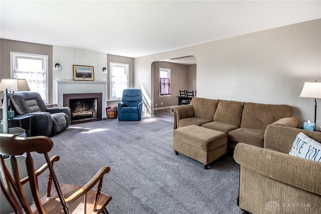 carpeted living room featuring a brick fireplace, baseboards, and arched walkways