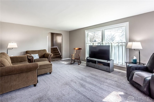 carpeted living room with arched walkways, stairway, and baseboards