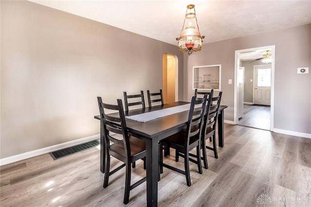 dining room featuring arched walkways, visible vents, light wood-style floors, ceiling fan, and baseboards