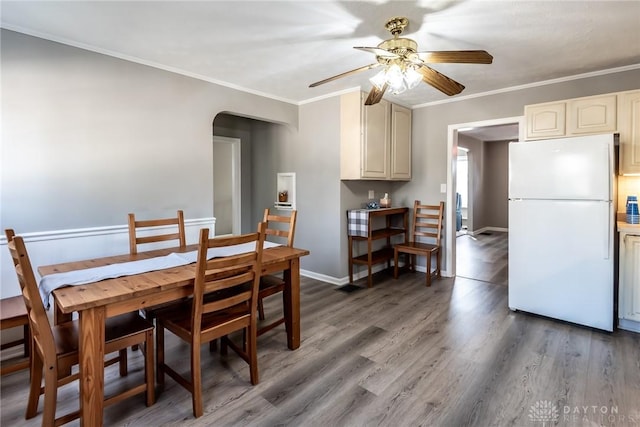 dining space featuring arched walkways, crown molding, a ceiling fan, light wood-type flooring, and baseboards