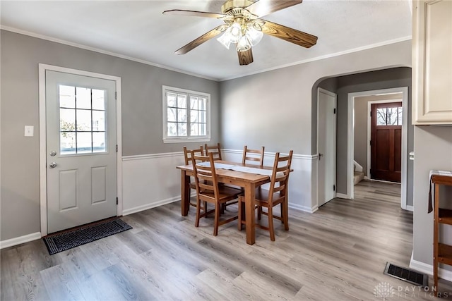 dining space featuring arched walkways, ceiling fan, light wood-style flooring, visible vents, and crown molding