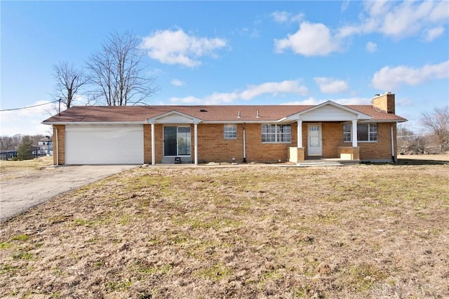 single story home featuring brick siding, a chimney, an attached garage, a front yard, and driveway