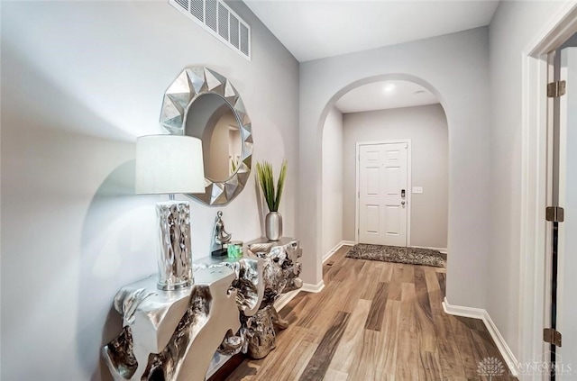 interior space with arched walkways, baseboards, visible vents, and light wood finished floors