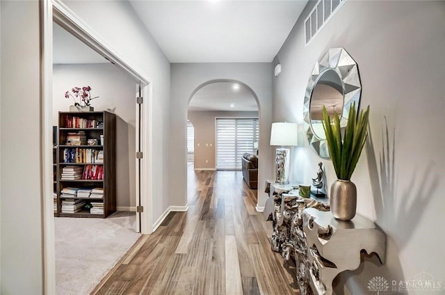 corridor with arched walkways, wood finished floors, visible vents, and baseboards