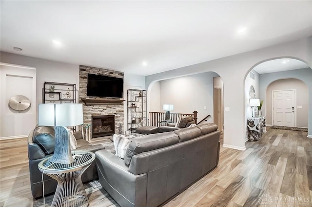 living room with baseboards, arched walkways, a stone fireplace, light wood-type flooring, and recessed lighting