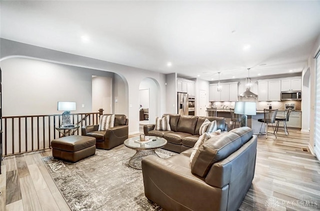 living room featuring light wood-style floors, arched walkways, and recessed lighting