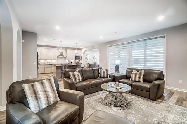 living area featuring arched walkways, baseboards, wood finished floors, and recessed lighting