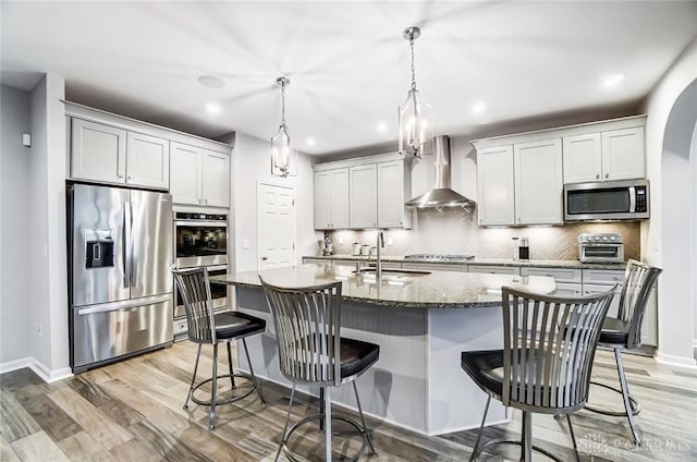 kitchen with wall chimney exhaust hood, appliances with stainless steel finishes, a sink, light wood-type flooring, and backsplash