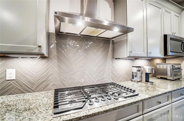 kitchen with light stone counters, a toaster, stainless steel appliances, backsplash, and wall chimney range hood