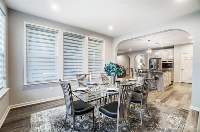 dining area featuring light wood-type flooring, baseboards, arched walkways, and a wealth of natural light