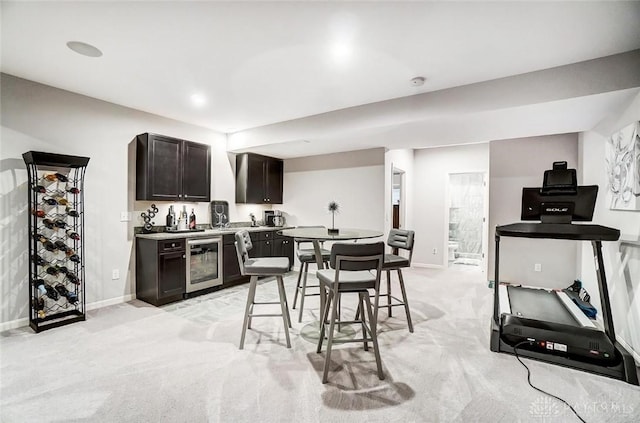 kitchen with dark brown cabinetry, beverage cooler, baseboards, light colored carpet, and light countertops