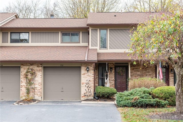 townhome / multi-family property featuring aphalt driveway, brick siding, a shingled roof, and an attached garage