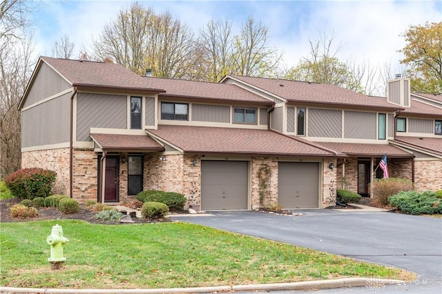 multi unit property with brick siding, a chimney, a garage, driveway, and a front lawn