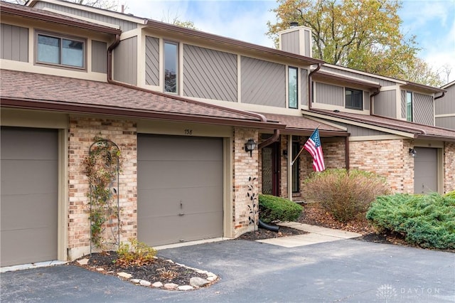 exterior space with a garage, brick siding, a chimney, and aphalt driveway