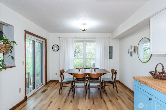 dining room featuring a textured ceiling, light wood finished floors, visible vents, and baseboards