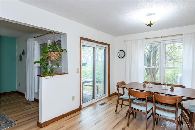 dining space featuring a healthy amount of sunlight, visible vents, light wood finished floors, and a textured ceiling