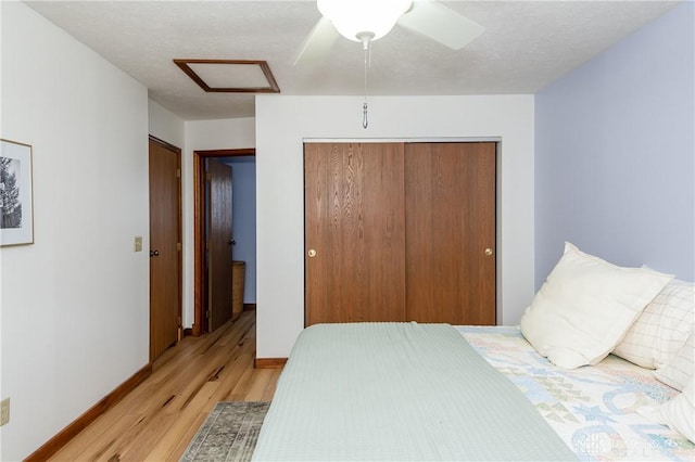 bedroom with a textured ceiling, ceiling fan, baseboards, light wood finished floors, and attic access