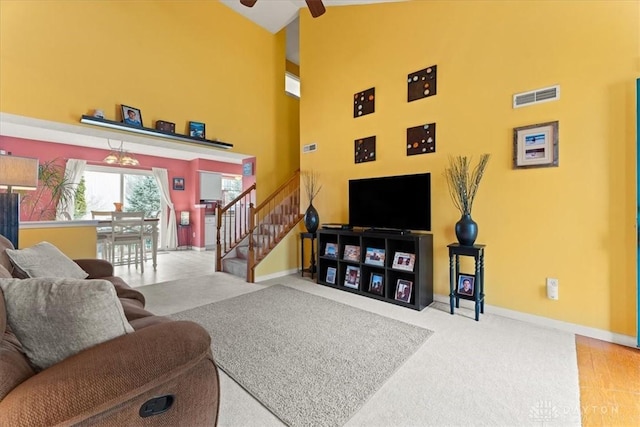 carpeted living room featuring visible vents, a towering ceiling, a ceiling fan, baseboards, and stairs