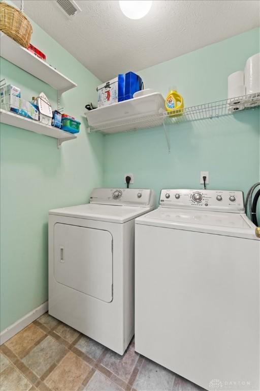 laundry room featuring a textured ceiling, washing machine and dryer, laundry area, visible vents, and baseboards