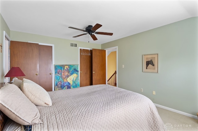 bedroom with baseboards, visible vents, ceiling fan, carpet, and two closets