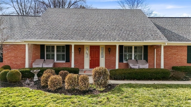 view of front of house featuring a shingled roof, a front lawn, a porch, and brick siding