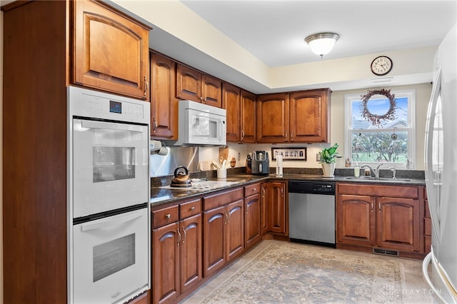 kitchen featuring white appliances, brown cabinetry, and a sink