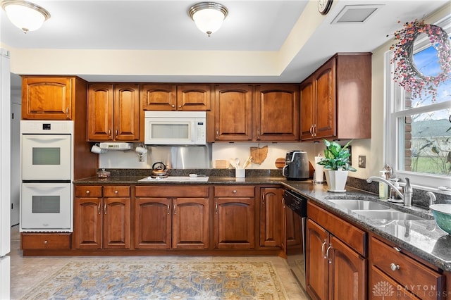 kitchen featuring white appliances, dark stone counters, a sink, and brown cabinetry