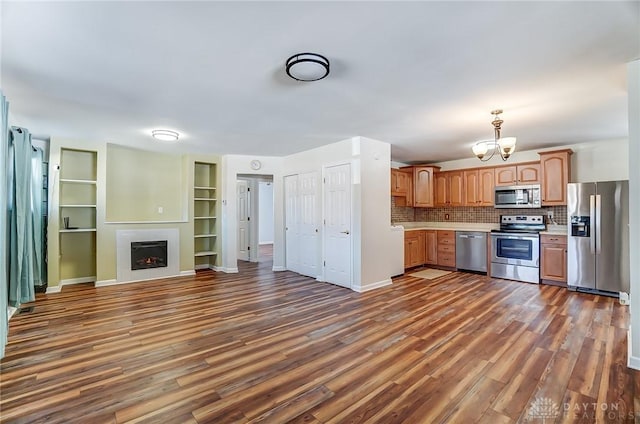 kitchen featuring stainless steel appliances, open floor plan, light countertops, a lit fireplace, and dark wood-style floors