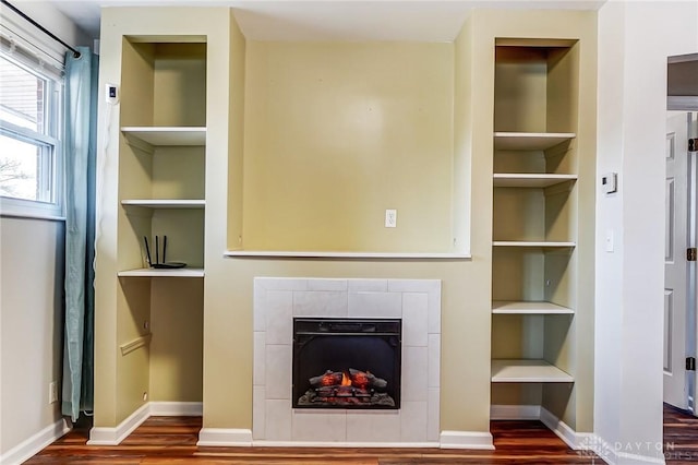 unfurnished living room featuring a tile fireplace, baseboards, and wood finished floors