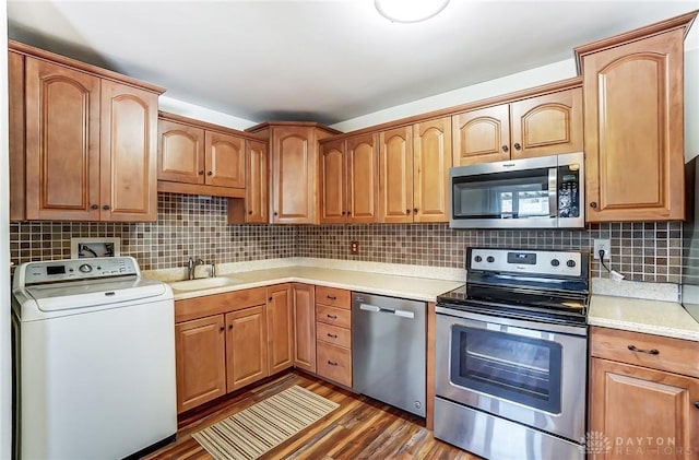 kitchen with washer / dryer, appliances with stainless steel finishes, wood finished floors, a sink, and backsplash