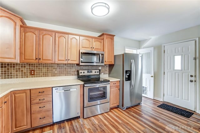 kitchen with light countertops, appliances with stainless steel finishes, light wood-style flooring, and decorative backsplash