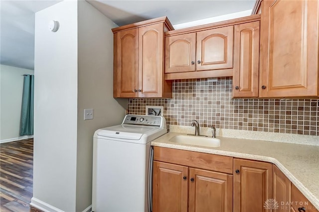 clothes washing area featuring wood finished floors, a sink, baseboards, cabinet space, and washer / dryer