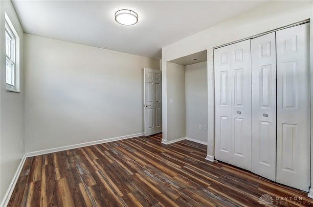 unfurnished bedroom featuring a closet, dark wood finished floors, and baseboards