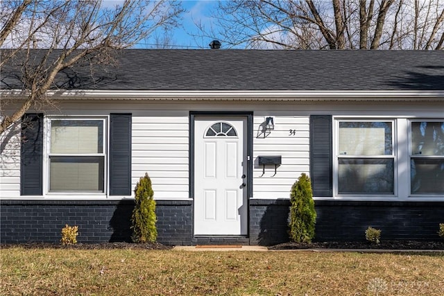 property entrance featuring roof with shingles, brick siding, and a lawn