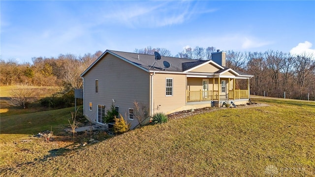 rear view of house featuring a chimney, a porch, and a lawn